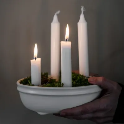 Adventsljusstake i glaserat naturvitt stengods från Ernst dekorerad med tända ljus och mossa.